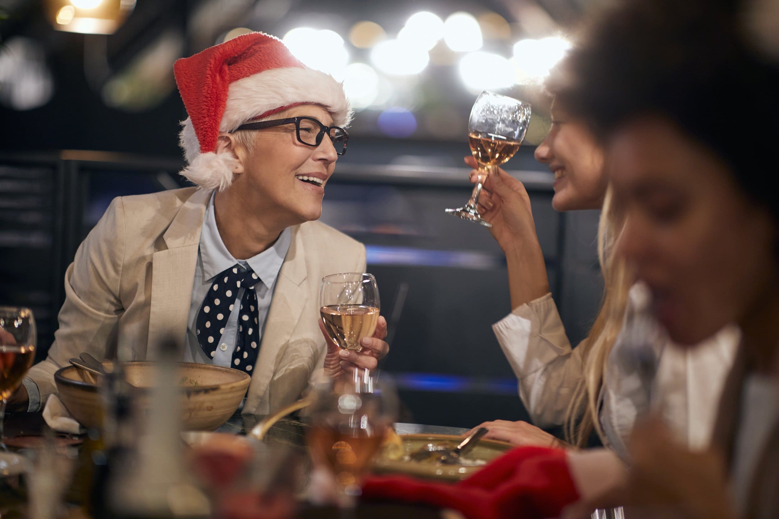 caucasian boss lady wearing santa hat with glasses having a good time at business dinner at the end of successful year with colleagues